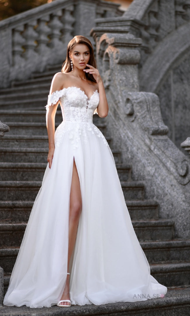 Eine Braut, die ein „Elegant Eminence“ A-Linien-Brautkleid mit Herzausschnitt und Tüllschlitz von „Susannas Brautmode“ in Leverkusen trägt, verkörpert moderne Eleganz und sinnliche Raffinesse.