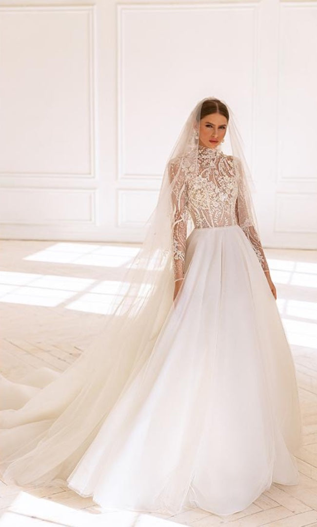 Eine elegante Braut in einem A-Linien Kleid mit Spitzenoberteil, langen Ärmeln und fließendem Rock, ergänzt durch einen klassischen langen Schleier.