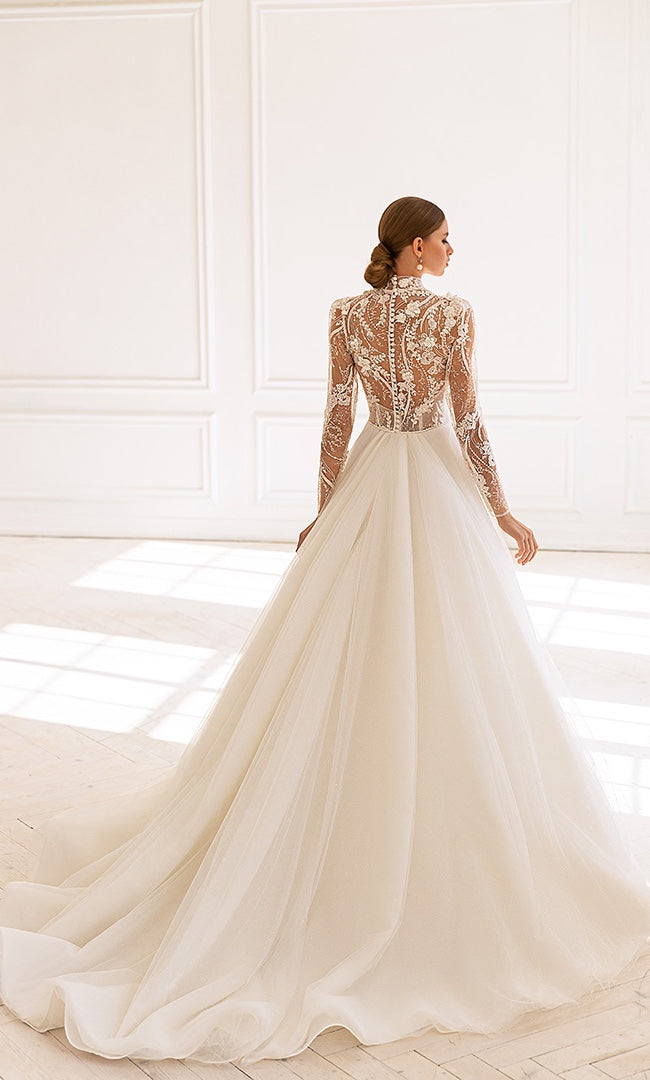 Rückansicht einer Braut im A-Linien Hochzeitskleid mit detailreicher Spitze und verdeckten Knöpfen, die zu einem ausladenden Tüllrock mit Schleppe übergehen.