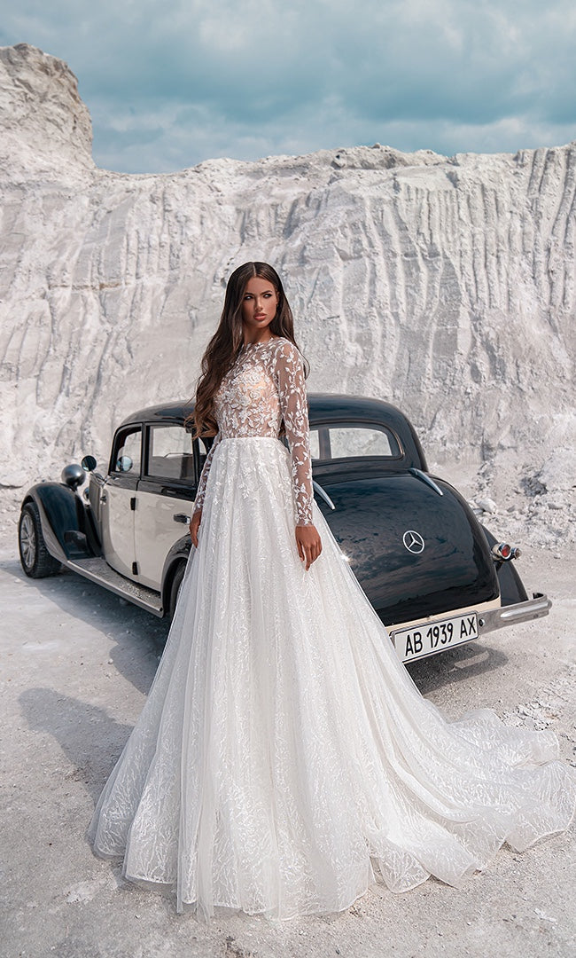 Eine Braut  trägt das „Valentina“ A-Linie Brautkleid von „Susannas Brautmode“ mit langen Ärmeln und filigraner Stickerei, vor einer atemberaubenden weißen Kreidefelsenkulisse, das Eleganz und moderne Romantik ausstrahlt.